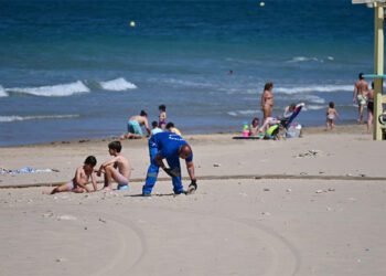 Operario retirando piedras entre los primeros bañistas de junio / FOTO: Eulogio García