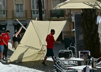 Camareros luchando con una sombrilla caída por el viento en una terraza / FOTO: Eulogio García